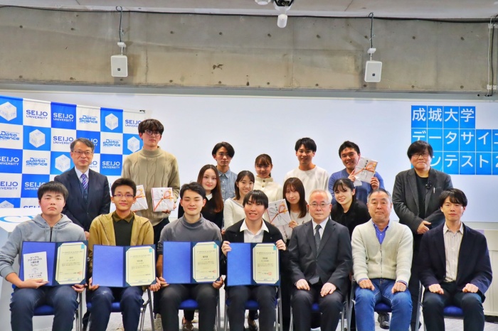 一瞬、マスクを外して全体撮影。学生諸君は決勝戦進出3チームの皆さん。1列目。右から山田隆史様(ピープルアナリティクス&HRテクノロジー協会)、増川経済学部長、戸部学長。2列目。左端は辻特任教授(データサイエンス教育研究センター)、右端は小宮路データサイエンス教育研究センター長。